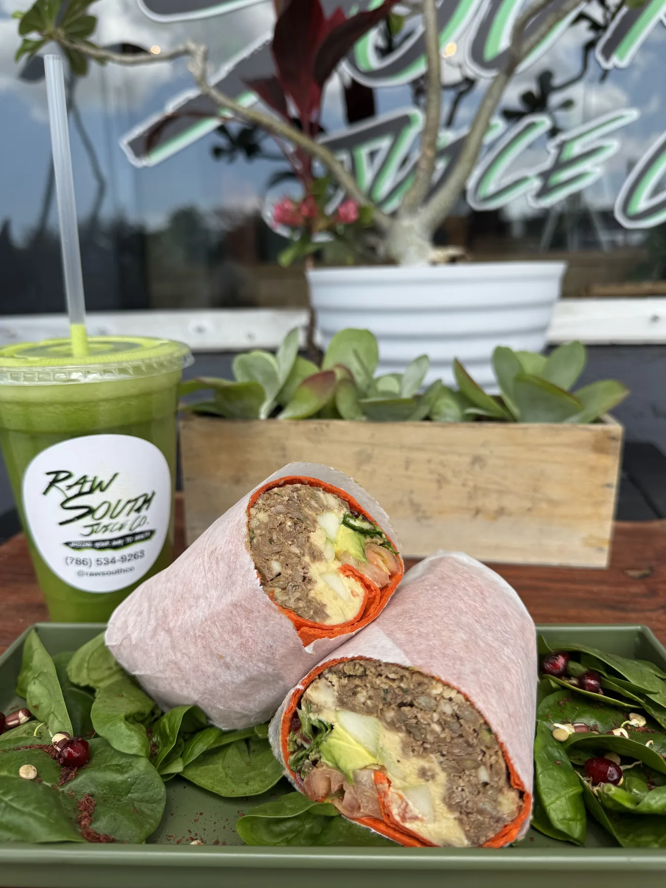 Raw South wrap and juice displayed with the café logo in the background.